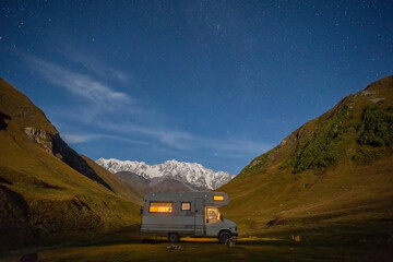mobile home in the mountains against the backdrop of a snowy peak, starry sky
