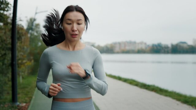 Young Athlete Asian Girl Running and Looking at Smart Watch Outdoor to Calculate the Calories. Fitness Workout Equipment App Technology Active Device