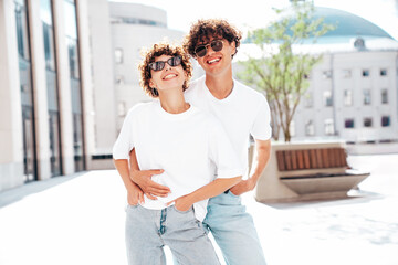 Young smiling beautiful woman and her handsome boyfriend in casual summer white t-shirt and jeans clothes. Happy cheerful family. Female having fun. Couple posing in street at sunny day. In sunglasses