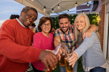 selfie photograph of a multigenerational and multiethnic group posing with their beers on the terrace of their house