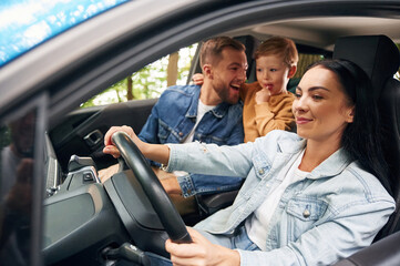 Cheerful people driving. Family of father, mother and little son are sitting in the modern car