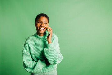 Happy young woman talking on a green phone and wearing green clothes in front of a green background...