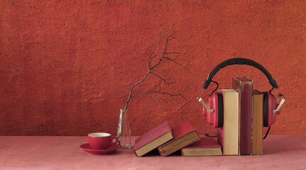 Relaxing with audiobooks concept with heap of books and vintage headphones. Red background with...