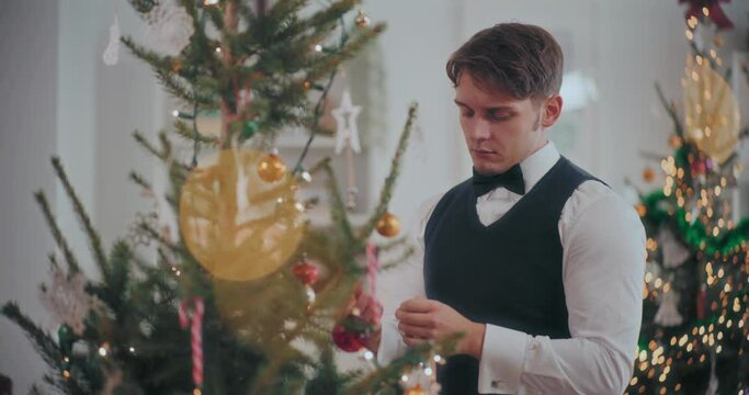 Young man in tuxedo decorating Christmas tree at home