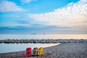 beach chairs looking out from kew beach with a tiny tug boat on distant horizon blue sky white...