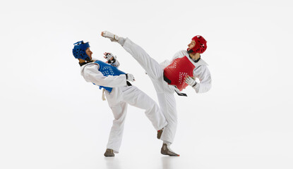 Two men in kimono and helmets practicing taekwondo, training, fighting isolated over white background. Concept of martial arts, combat sport, competition, action, strength, education