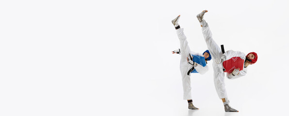 Flexible, athletic young men, taekwondo athletes in kimono and helmet training isolated over white background. Concept of martial arts, combat sport, competition, action, strength, education. Banner