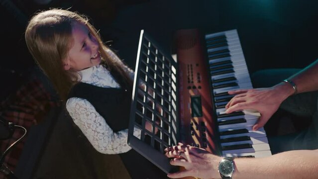 Child masters craft of vocal with mentor. Tiny girl student refines singing abilities with instructor playing synthesizer upper view. Musical development