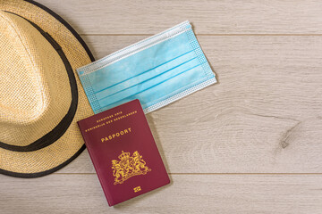 Summer hat with mouth mask and Dutch passport on wooden background. straw hat, passport and mouth...