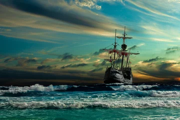 Foto auf Glas Grand view of an old sailing ship from the times of pirates and the Middle Ages on the high seas with big waves and with a beautiful sky © proslgn