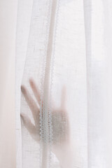 Hand opening white window curtains in room, closeup. Space for text. Bright morning sun through the curtains