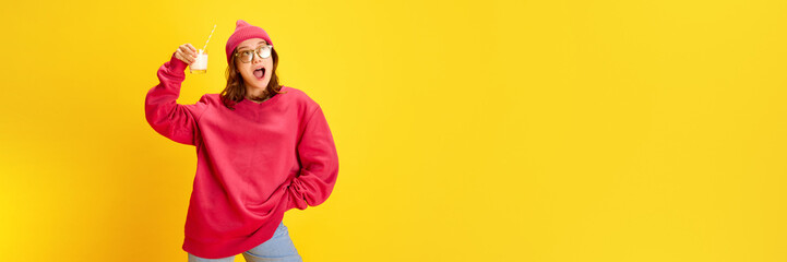 Banner. Young attractive happy lady holds milk cocktail with straw against yellow background with negative space to insert your text. Concept of fashion and style, traveling, culture, fun and joy. - obrazy, fototapety, plakaty