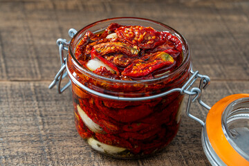 Sun-dried red tomatoes with garlic, olive oil and spices in a glass jar on a wooden table. Rustic...