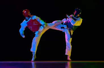 Poster Competitive strong young men, taekwondo, karate athletes in motion, fighting, training against black background in neon light. Concept of martial arts, combat sport, competition, action, strength © master1305