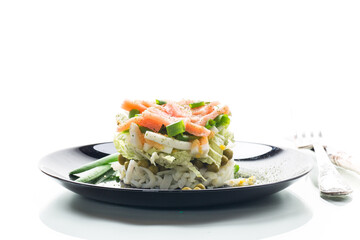 Layered salad of cabbage and other vegetables with pieces of red fish in a plate.