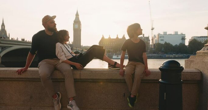 Handsome father together with teenage daughter and son enjoy beautiful sunset near Thames with the view of Big Ben