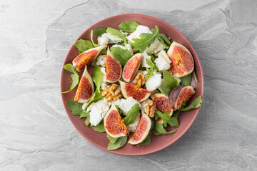 Tasty salad with sliced figs, crushed soft goat cheese, walnut and fresh arugula leaves on red...