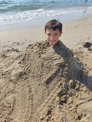Portrait of a smiling boy playing buried up to his neck in sand