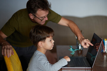 Father helps his son use a laptop. 