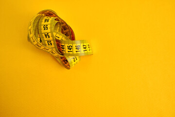 Yellow measuring tape on a yellow background. Tool for measuring length and volume. Tape for measuring in the clothing industry or the volume of the human body