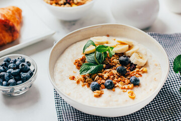 close-up on a plate with oatmeal, banana, mint berries on a background of dishes on a white table