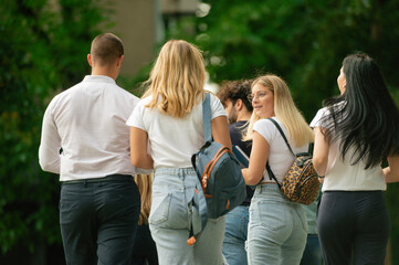 Young group of students with backpacks and notebooks walking outside to their school together