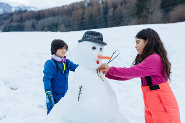 two girls making snowman on top of snowy mountain