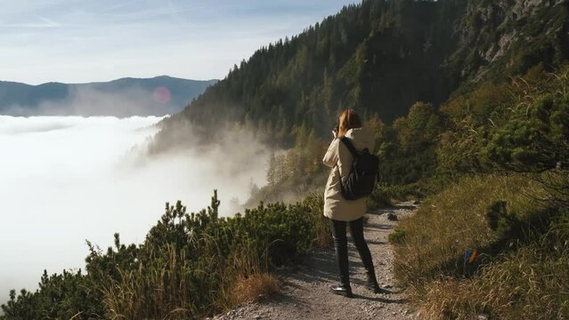 Beautiful female traveler walks through the forest to the mountains higher than clouds and takes pictures of mountains Incredibly beautiful views in the Alpine mountains. Hiking route in the Alps