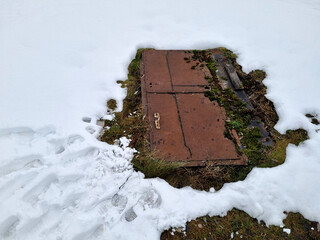 Post-apocalypse. Winter.  Old rusty iron door in the snow on the ground in winter. Entrance to the shelter, covering the traces of people entering the door