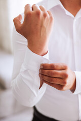 handsome business man buttoning shirt sleeves at home. The groom is preparing for the wedding. Close-up photo.