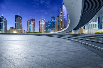 Empty square floor and pedestrian bridge with modern city commercial buildings at night in...