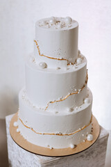 A large luxurious multi-tiered wedding cake is decorated with white pearls in the banquet hall. Wedding dessert under the evening light. Wedding decor.