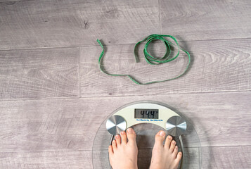 A woman measures her weight. There are floor scales on the floor and a measuring tape, the concept...