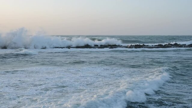 Large waves in the Mediterranean Sea crash against the rocks, depicting a scene of stormy weather at sea.