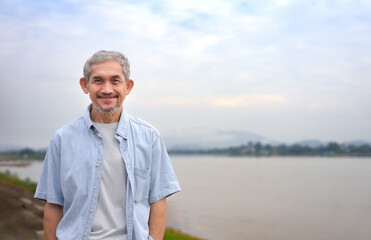 portrait asian senior man standing beside Mekong River,mature male traveling destination Golden Triangle, Chiang Rai,Thailand,concept elderly pensioner people lifestyle,holiday,travelling - obrazy, fototapety, plakaty