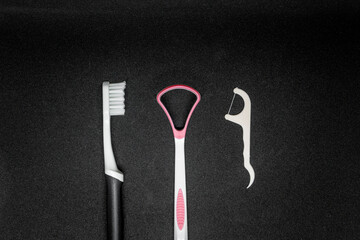 A toothbrush, a tongue scraper and a dental floss on black background