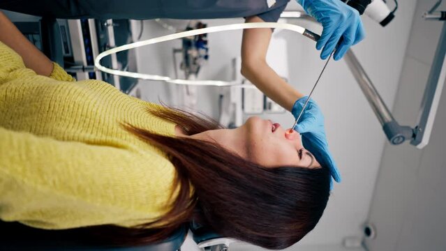 vertical video the ENT doctor performs the procedure of endoscopy of the patient's nose in the clinic holding a professional device in his hand
