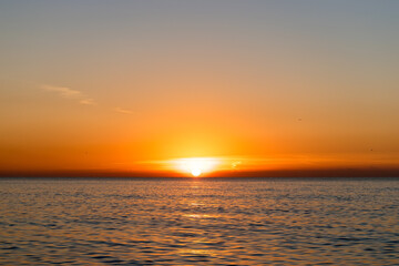 Bright sunset with a big yellow sun above the sea surface.
