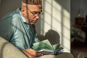 Lifestyle portrait of senior islamic man reading Quran at home. Natural aesthetic light