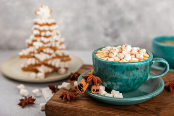 Hot drink with marshmallows and candy cane in blue cup on texture table.Cozy seasonal holidays.Hot cocoa with gingerbread Christmas cookies.Hot chocolate with marshmallow and spices.Copy space.