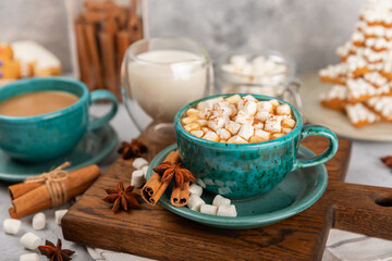Hot drink with marshmallows and candy cane in blue cup on texture table.Cozy seasonal holidays.Hot cocoa with gingerbread Christmas cookies.Hot chocolate with marshmallow and spices.Copy space.
