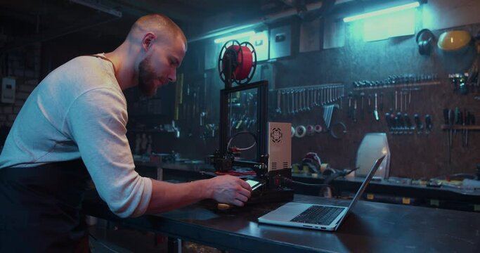 Professional male engineer using computer and 3D printer
