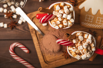 Obraz na płótnie Canvas Hot drink with marshmallows and candy cane in a red cup on a texture table.Cozy seasonal holidays.Hot cocoa with gingerbread Christmas cookies.Hot chocolate with marshmallow and spices.Copy space.