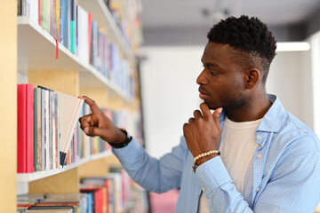 A serious and contemplative student in the library, surrounded by books, absorbed in academic...
