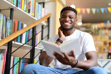 Happy young student in a library, surrounded by books and knowledge, exuding academic joy. - obrazy, fototapety, plakaty