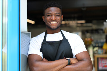 Smiling black entrepreneur, owner of a successful restaurant, confidently standing with crossed arms indoors.