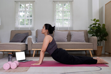 Fat Asian woman stretching at home on a fitness mat. Practicing activities at home online exercise classes Practice stretching on your yoga mat at home to stay healthy and in shape.