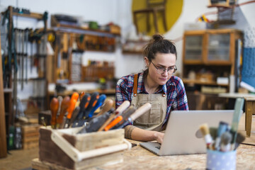 Young craftswoman using laptop in her workshop

