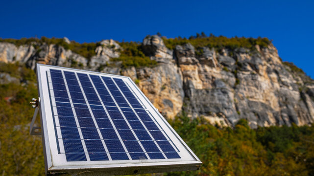 A solar panel in the foreground with a rocky mountain backdrop under a clear sky, depicting renewable energy in natural settings