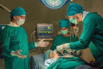 Team of surgery doctor using defibrillator pump chest heart patient to save life while medical surgery in operating room at emergency CPR. Defibrillator in surgeon specialist hand. - obrazy, fototapety, plakaty